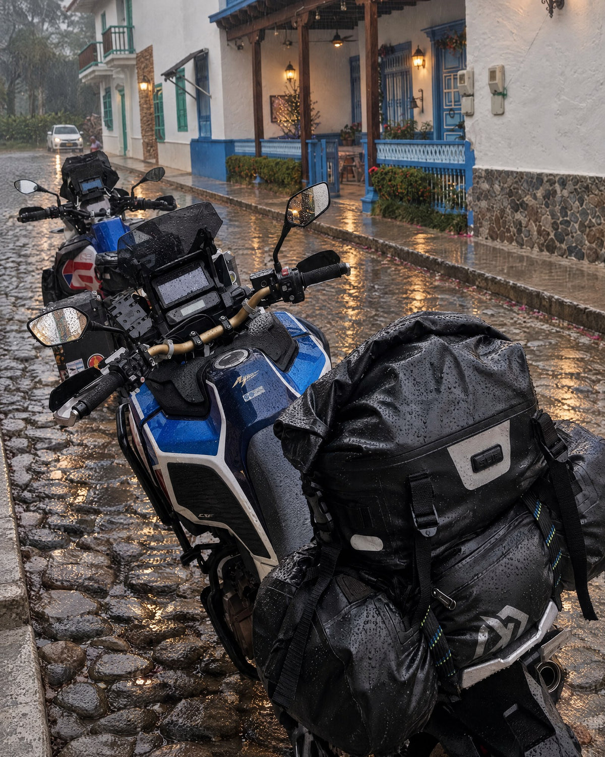 Moto con drybag Himalaya en una calle empedrada bajo la llovizna